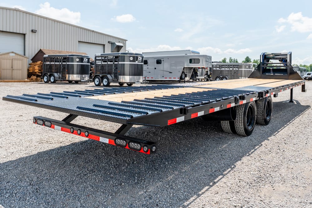 Flatbed car hauler trailer with loading ramps in an industrial yard on gravel.