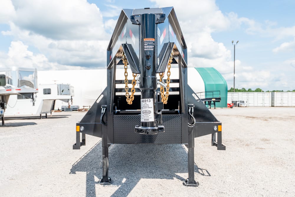 Front view of a heavy-duty gooseneck trailer hitch with safety chains in a gravel lot.