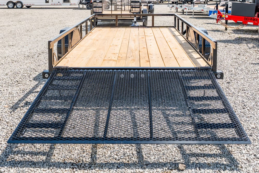 Flatbed trailer with a wooden deck and metal loading ramp in a gravel lot.