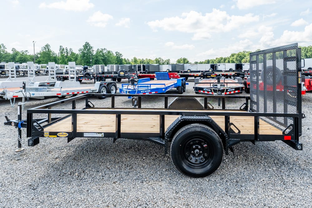 Black steel utility trailer with wooden deck and side rails, parked on a gravel lot.