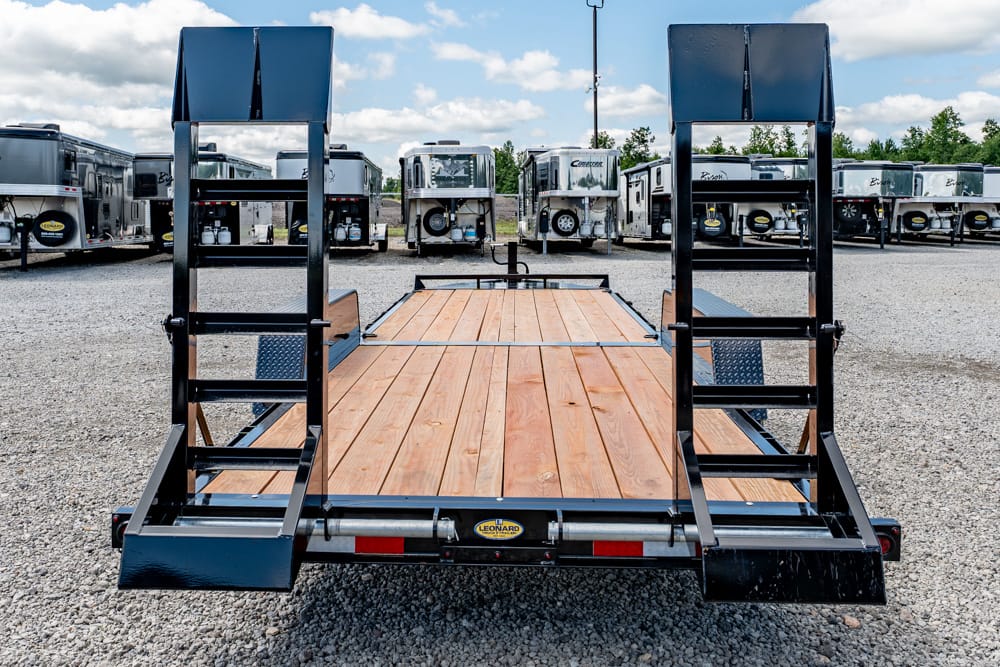 Flatbed trailer with wooden deck and raised rear ramps in a truck lot at an industrial yard.