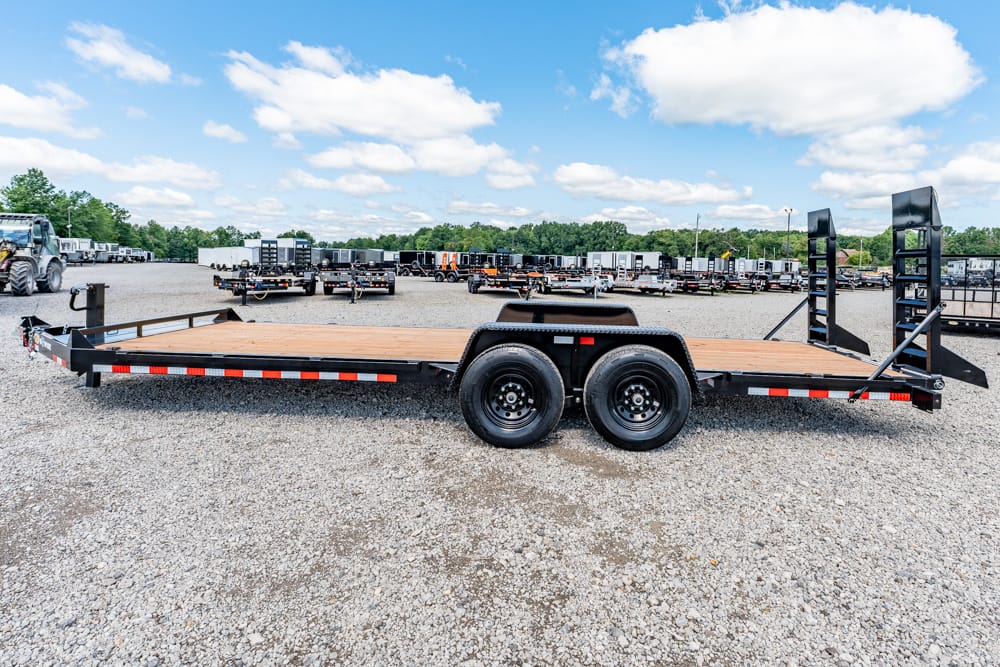 Black dual-axle flatbed trailer with a wooden deck parked on a gravel lot