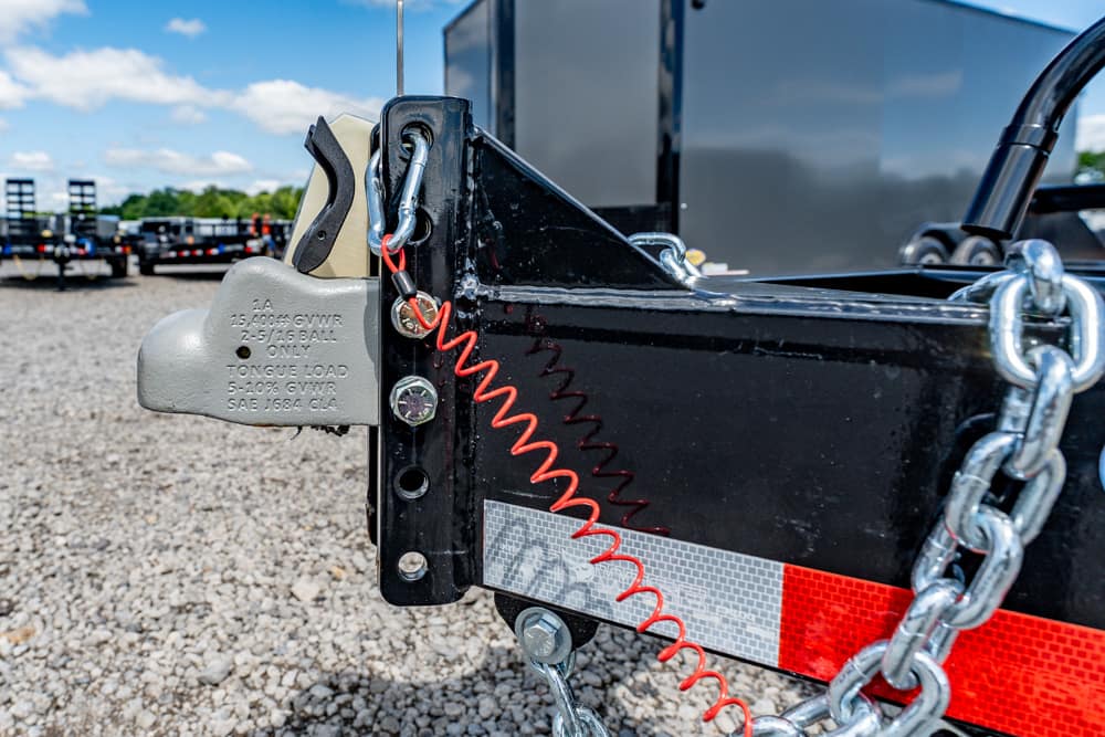 Close-up of a trailer hitch secured with a padlock, red coiled security cable, and metal safety chains.