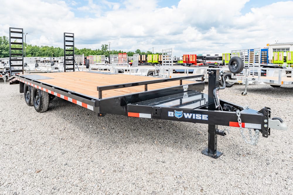 Flatbed trailer with a wooden deck and black steel frame on a gravel lot; hitch and chains visible, brand 'BOWISE' on the tongue.
