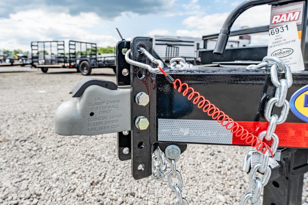 Close-up of a trailer hitch with a red coiled safety cable and metal chains securing a black frame pieces at a trailer neck.