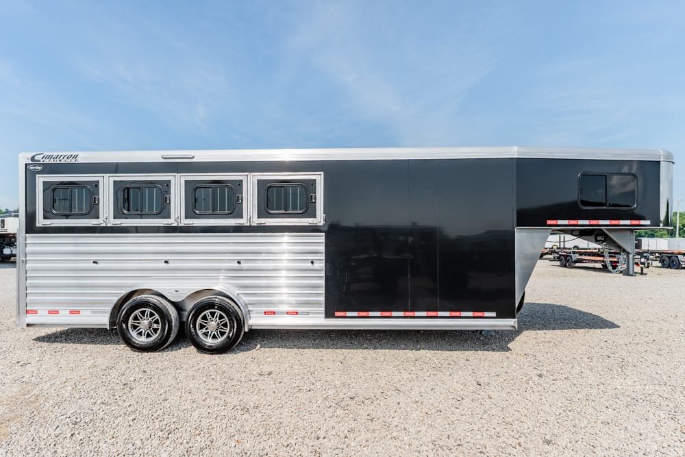 Two-tone horse trailer with silver lower panels and black upper section, four side windows, parked on a gravel lot with dual axles.