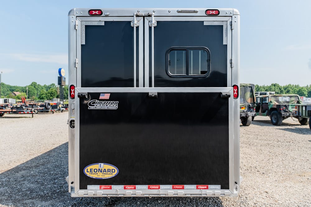 Back of a black horse trailer with silver-metal frame, small window, and rear lights visible; Leonard logo sticker at bottom left.