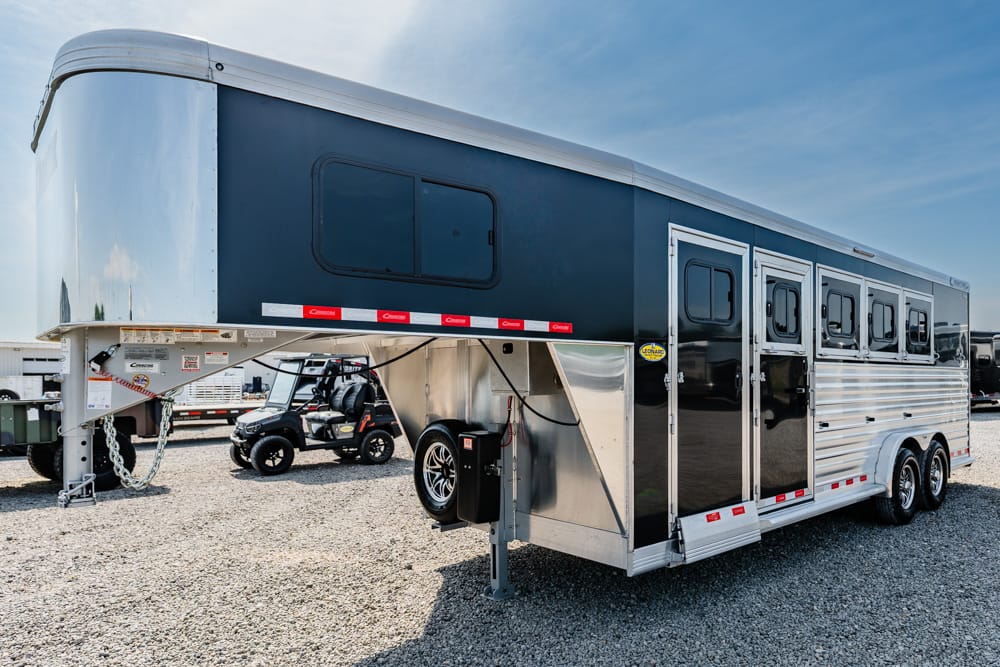 Two-tone gooseneck horse trailer with living quarters, black doors and multiple windows, parked on a gravel lot.