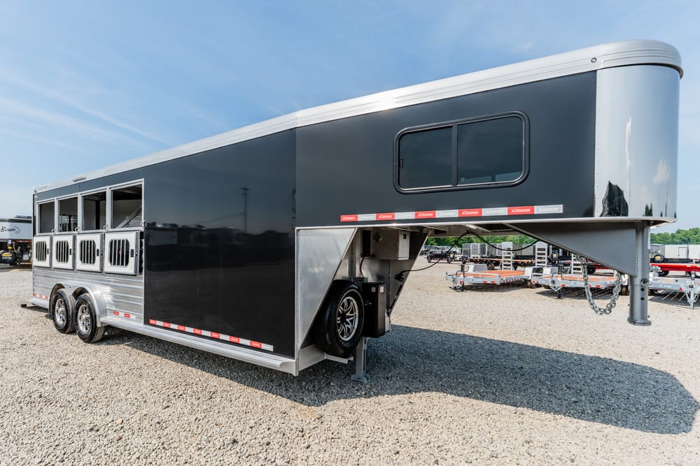 Black and silver gooseneck horse trailer with three stall doors, parked on a gravel lot.