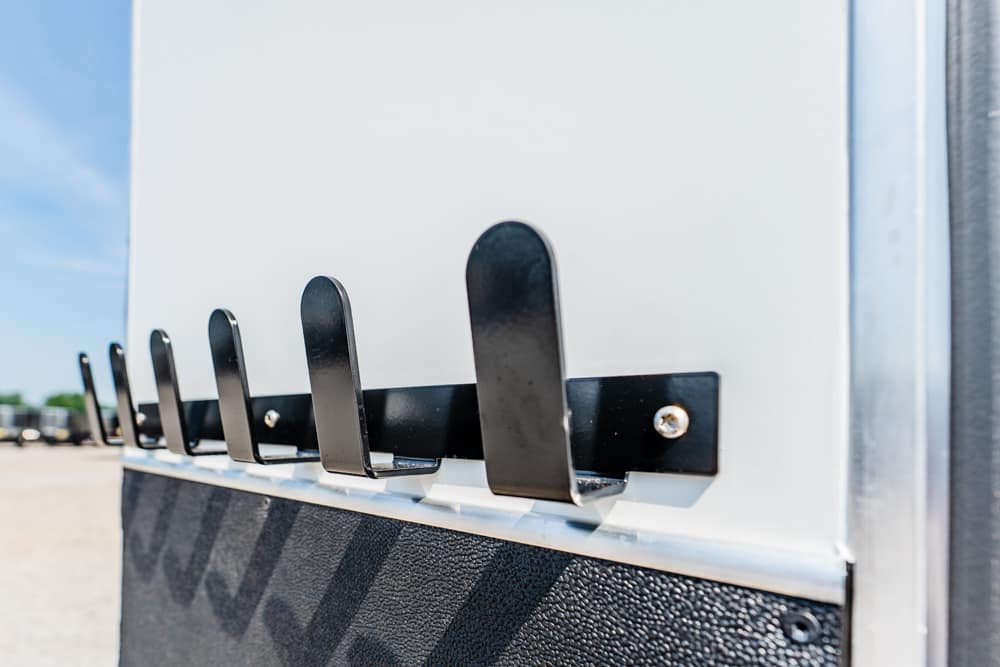 Row of black metal hooks mounted on a white panel of a utility trailer in an outdoor lot.