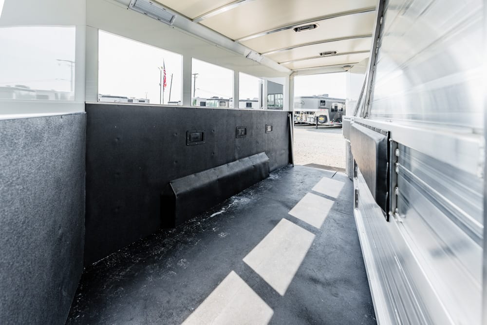 Interior of a long trailer with padded black side walls, a non-slip dark floor, and windows along the top; other trailers visible outside through the rear opening.