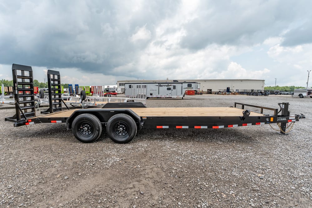 Black flatbed trailer with dual rear wheels and ramps on a gravel lot.