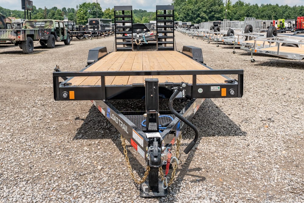 Flatbed trailer with a wooden deck in a gravel lot, surrounded by other trailers and vehicles.