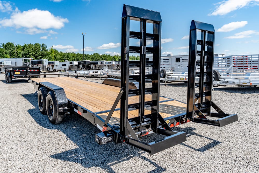 Flatbed trailer with a wooden deck and two tall black loading ramps raised at the rear in an outdoor trailer lot.