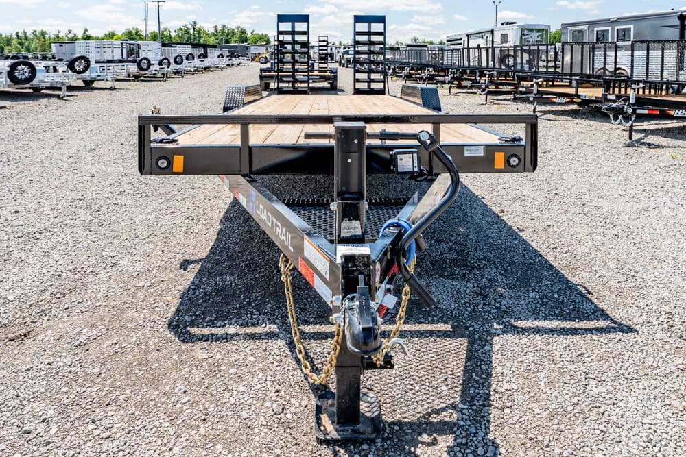 Front view of a black metal flatbed trailer hitch on a gravel lot with other trailers in the background.