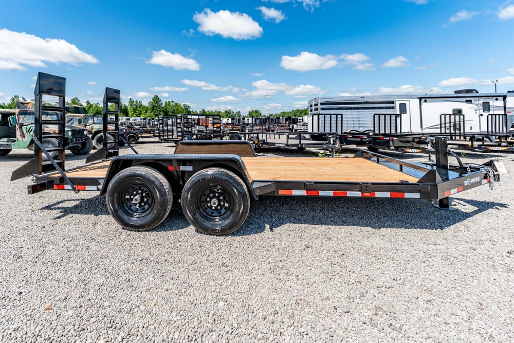Dual-axle flatbed trailer with a wooden deck parked on a gravel lot in a trailer yard.
