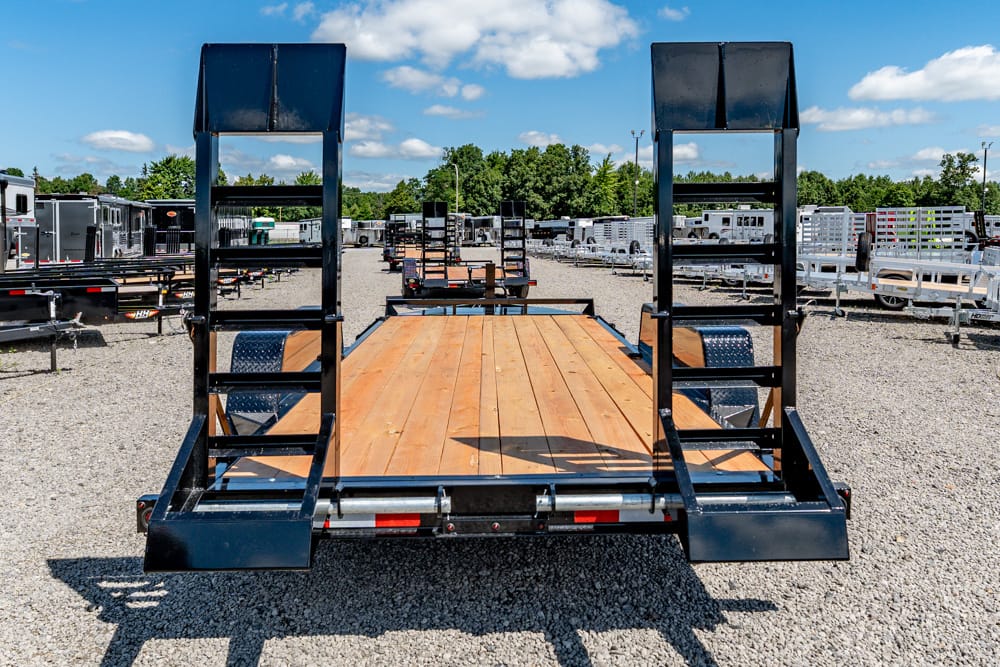 Flatbed trailer with wooden deck and dual rear ramps in a lot of trailers and equipment.