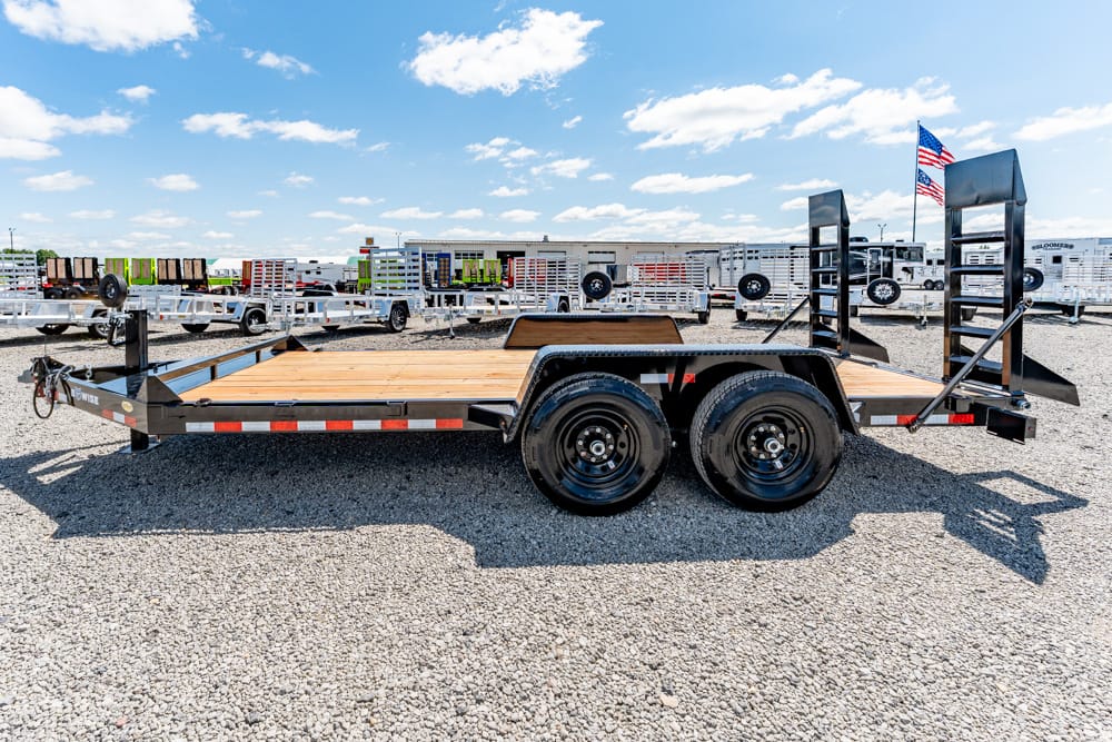 Dual-axle flatbed trailer with a wooden deck sitting on gravel in a trailer lot.