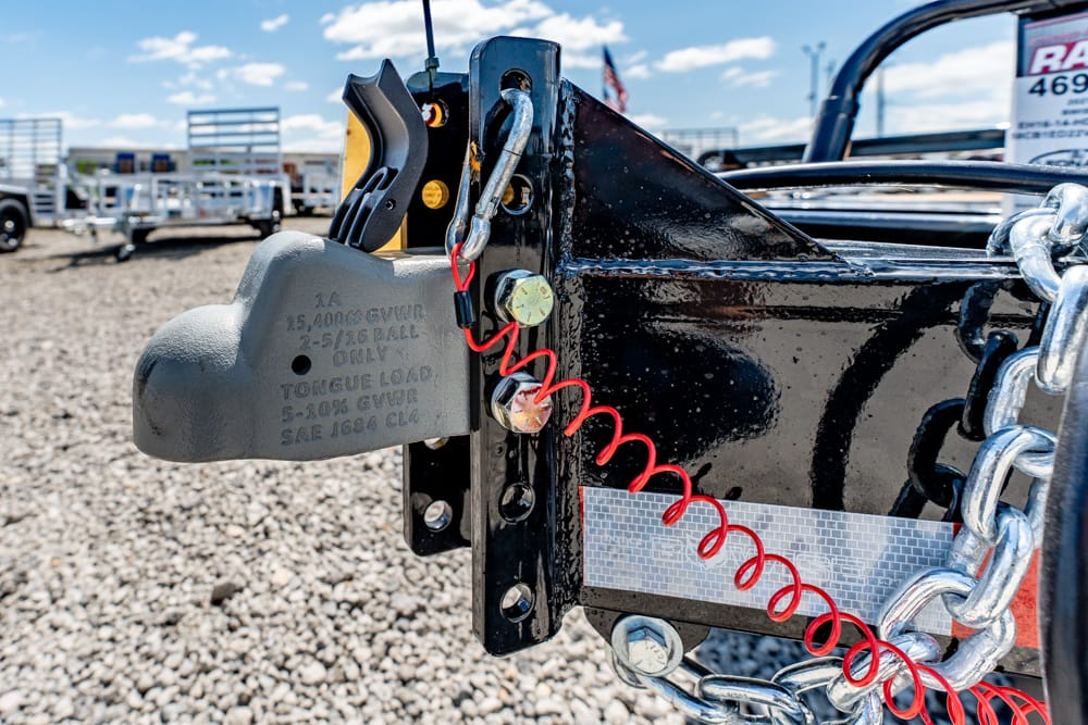 Close-up of a trailer hitch with a padlock, red coiled safety cable, and a metal chain on a black frame.