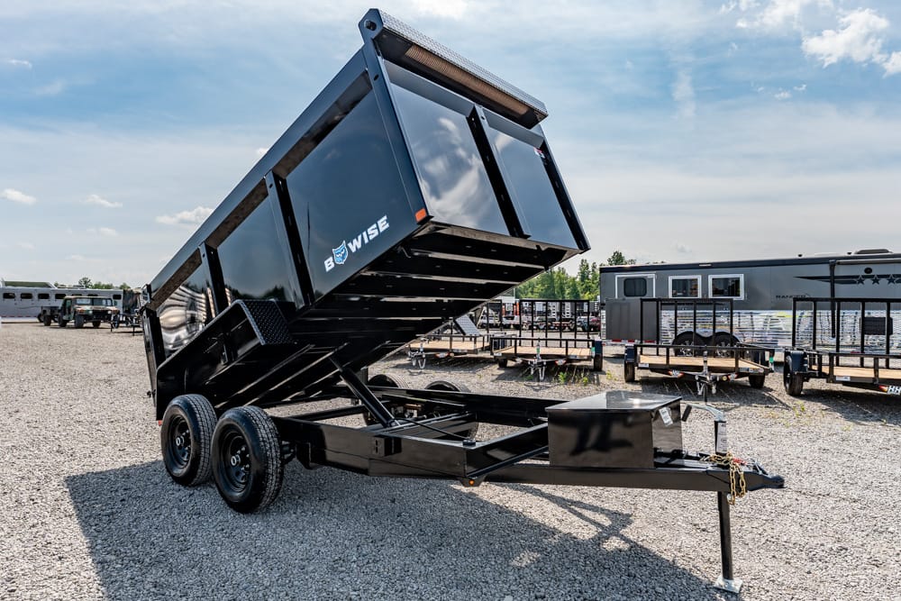 Black dump trailer tilted upward on its hydraulic bed at a gravel trailer yard.