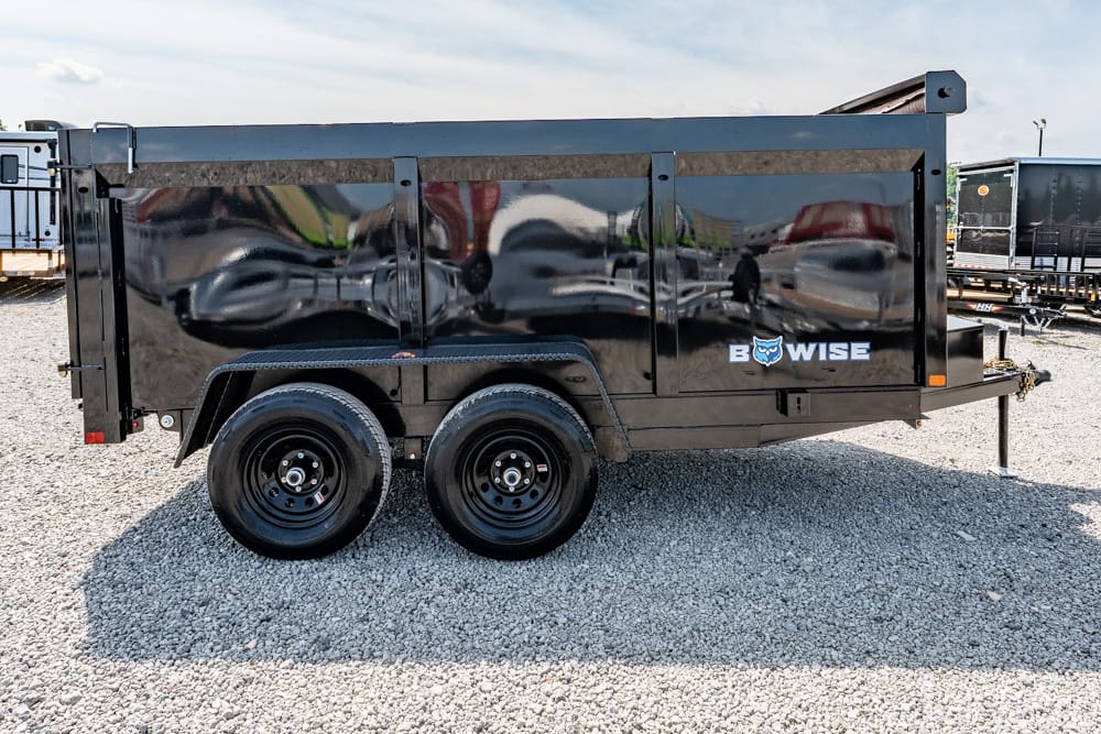 Black dual-axle dump trailer on a gravel lot, reflecting surroundings on its polished side, with a BOWISE logo and owl emblem on the side panel.