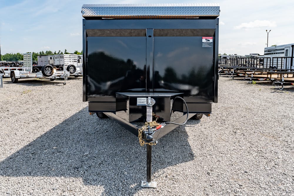 Front view of a black utility trailer on a gravel lot, showing the hitch, jack stand, and safety chains.