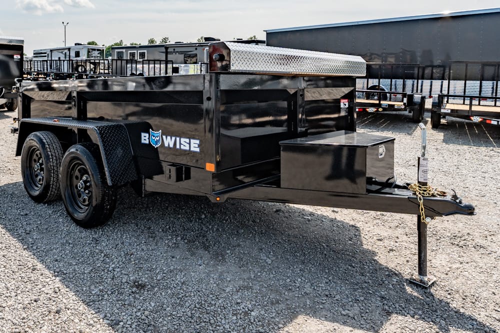 Black dual-axle utility trailer with a front jack and diamond-plate toolbox, labeled 'BOWISE' in a gravel lot.