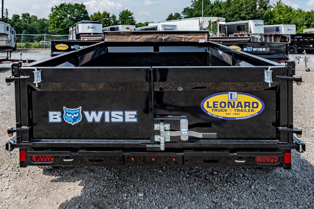 Rear view of a black dump trailer with the BWISE logo and Leonard Truck & Trailer badge on a gravel lot with other trailers in the background.