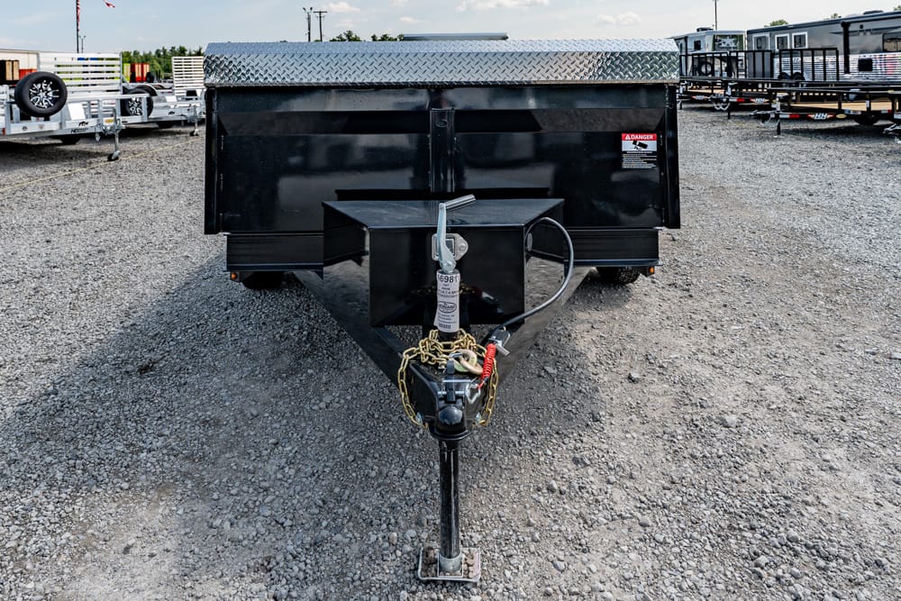 Front view of a black utility trailer on a gravel lot, showing the A-frame hitch with safety chains and a diamond-plate toolbox cover at the front.