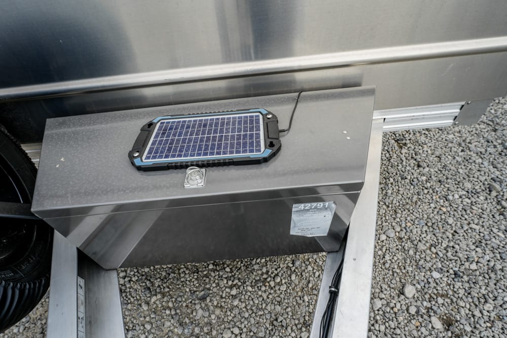 Solar panel resting on a gray metal toolbox mounted on a trailer, with gravel beneath.