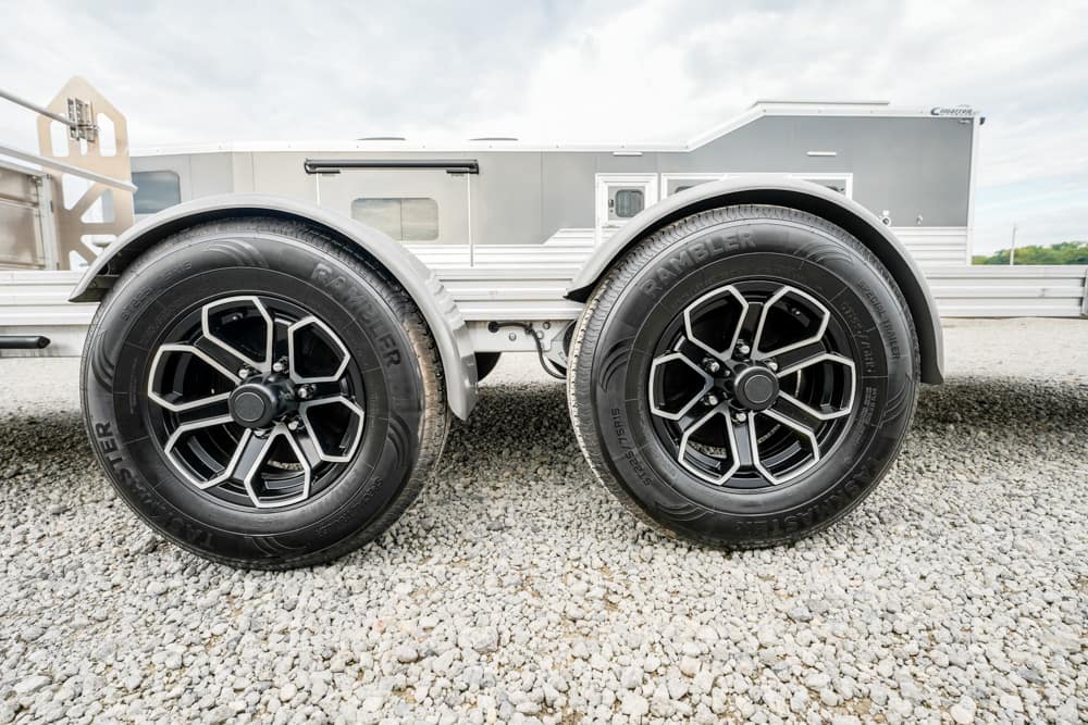 Twin-axle travel trailer wheels on a gravel lot, with gray aluminum siding in the background.