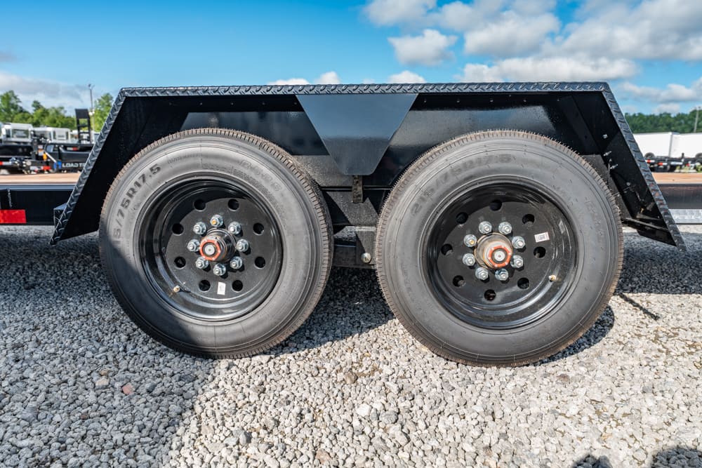Dual-axle trailer with black steel wheels on a gravel lot under a blue sky.
