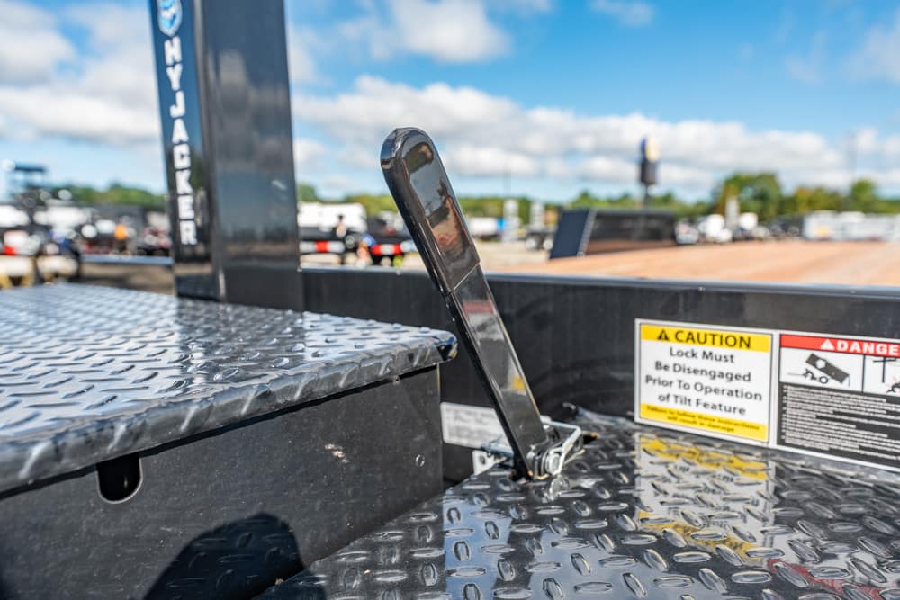 Close-up of a metal lever on a diamond-plate platform of a trailer, with yellow caution labels in the background.