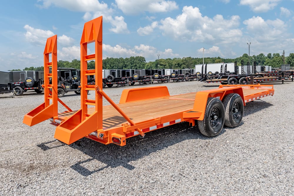 Bright orange heavy-duty car trailer with two tall rear ramps on a gravel lot, other trailers in the background.