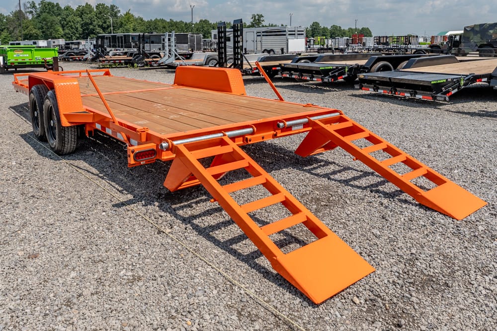 Orange flatbed trailer with fold-down loading ramps extended on a gravel lot, ready for equipment.