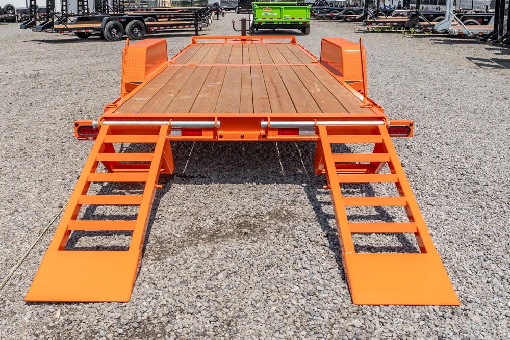 Orange flatbed trailer with two fold-down ramps on a gravel lot, ready to load equipment.