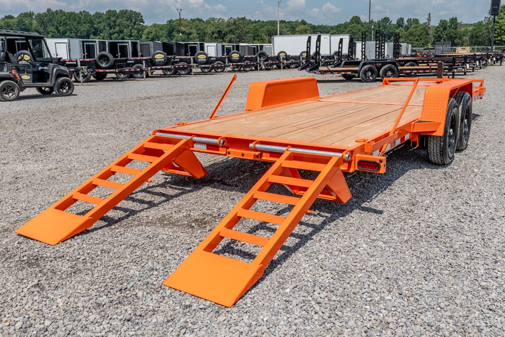 Orange dual-axle equipment trailer with lowered loading ramps on a gravel lot, ready for loading.