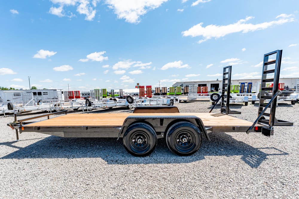 Flatbed trailer with dual rear axles parked on a gravel lot, with other trailers in the background under a blue sky.