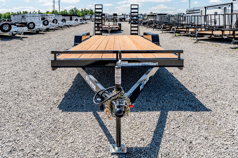 Front view of a flatbed trailer with a wooden deck, centered in a gravel trailer yard with rows of trailers behind it.