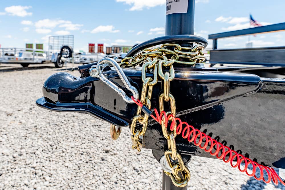 Close-up of a trailer hitch locked with chains and a red safety cable on a black trailer frame.