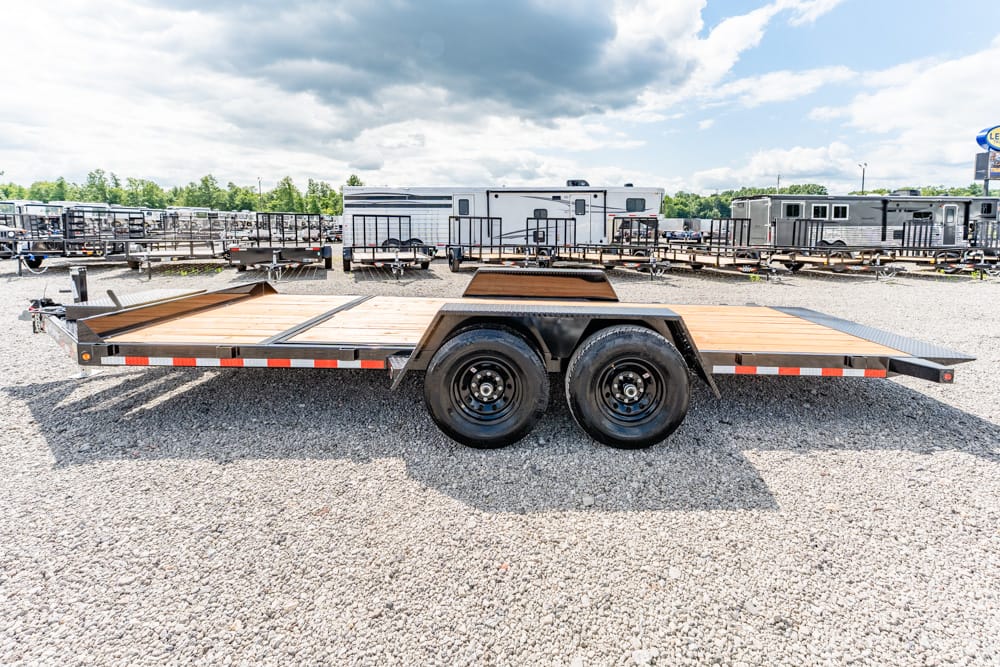 Dual-axle flatbed trailer with a wooden deck parked on a gravel lot, surrounded by other trailers.