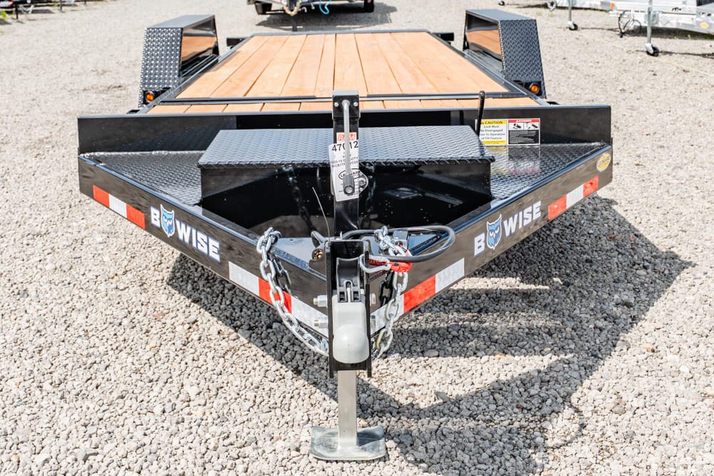 Black Wise flatbed trailer with a wooden deck, front hitch, chains, and a metal jack on a gravel lot