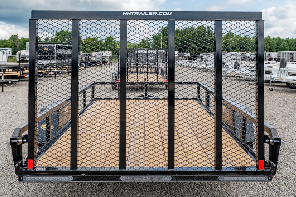 Rear view of a black utility trailer with a diamond mesh gate and wooden deck in a trailer lot.