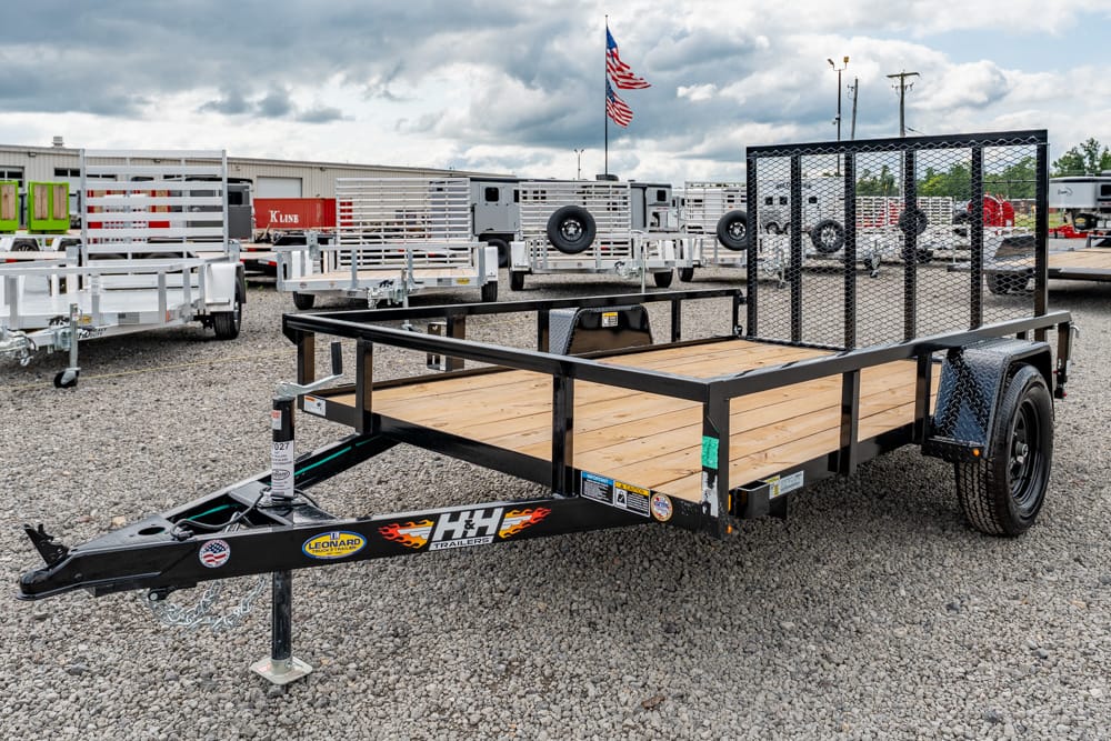 Black metal flatbed trailer with wooden deck and mesh rear gate in a trailer lot.