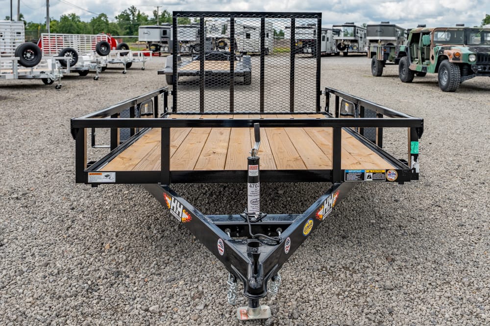 Flatbed utility trailer with a wooden deck and metal rails on a gravel lot, with other trailers in the background.
