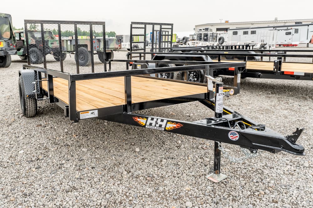 Flatbed utility trailer with wooden deck and metal rails in a gravel lot, ready for towing.