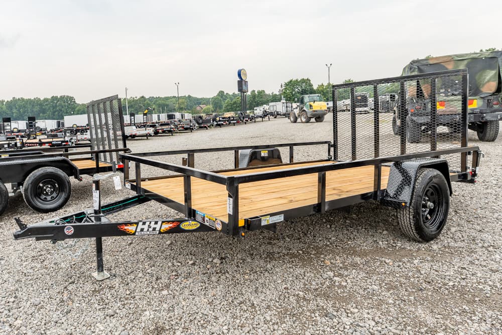 Black utility trailer with wooden deck and side rails in a gravel lot