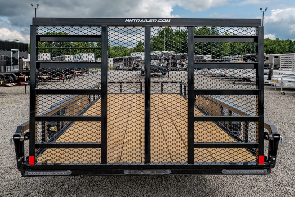 Rear view of a black dual-axle utility trailer with mesh gates and wood deck on a gravel lot, brand HHTrailer.com visible on top rail.