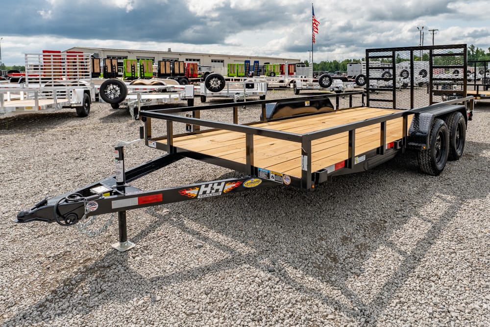 Two-axle flatbed trailer with a wooden deck and metal frame parked on a gravel lot among other trailers.