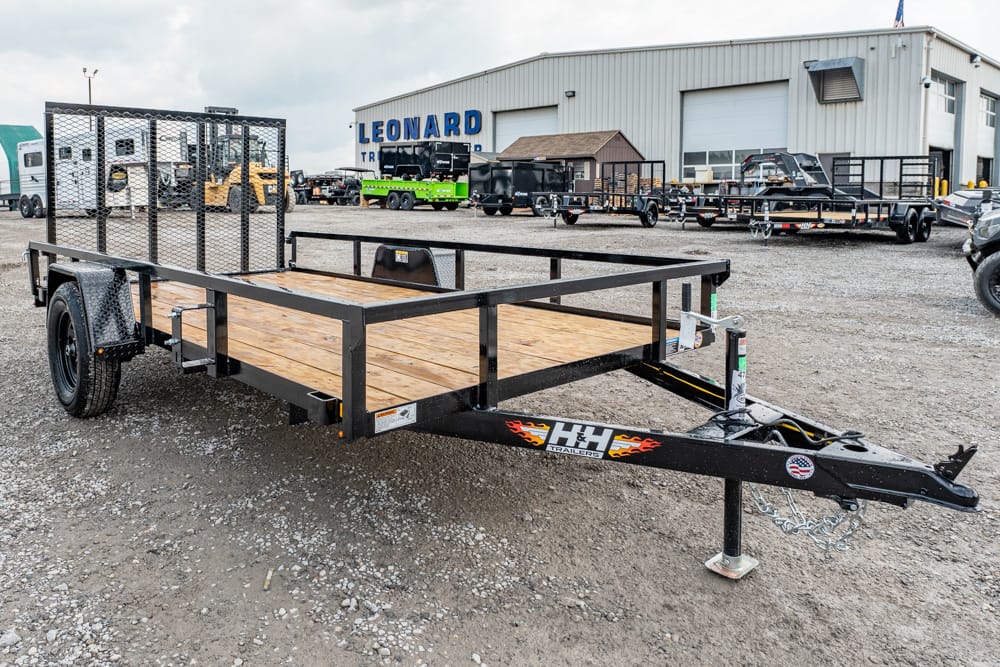 Flatbed trailer with wooden deck and metal rails parked on a gravel lot near a shop building labeled Leonard in the background.